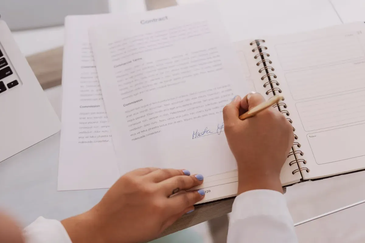 Mains qui signent un document relié.